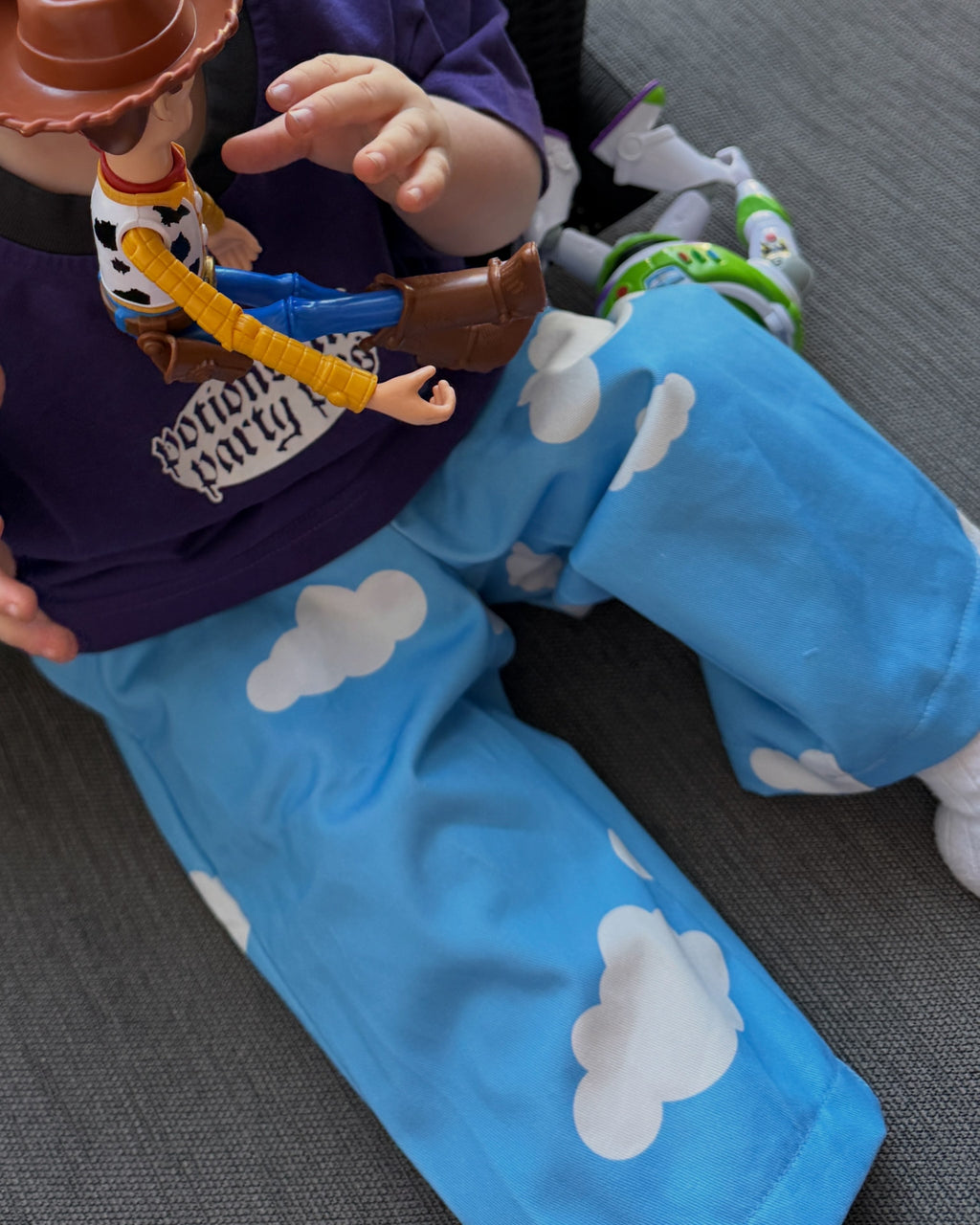 Child wearing blue pants with cloud pattern and a toy figure on a gray surface