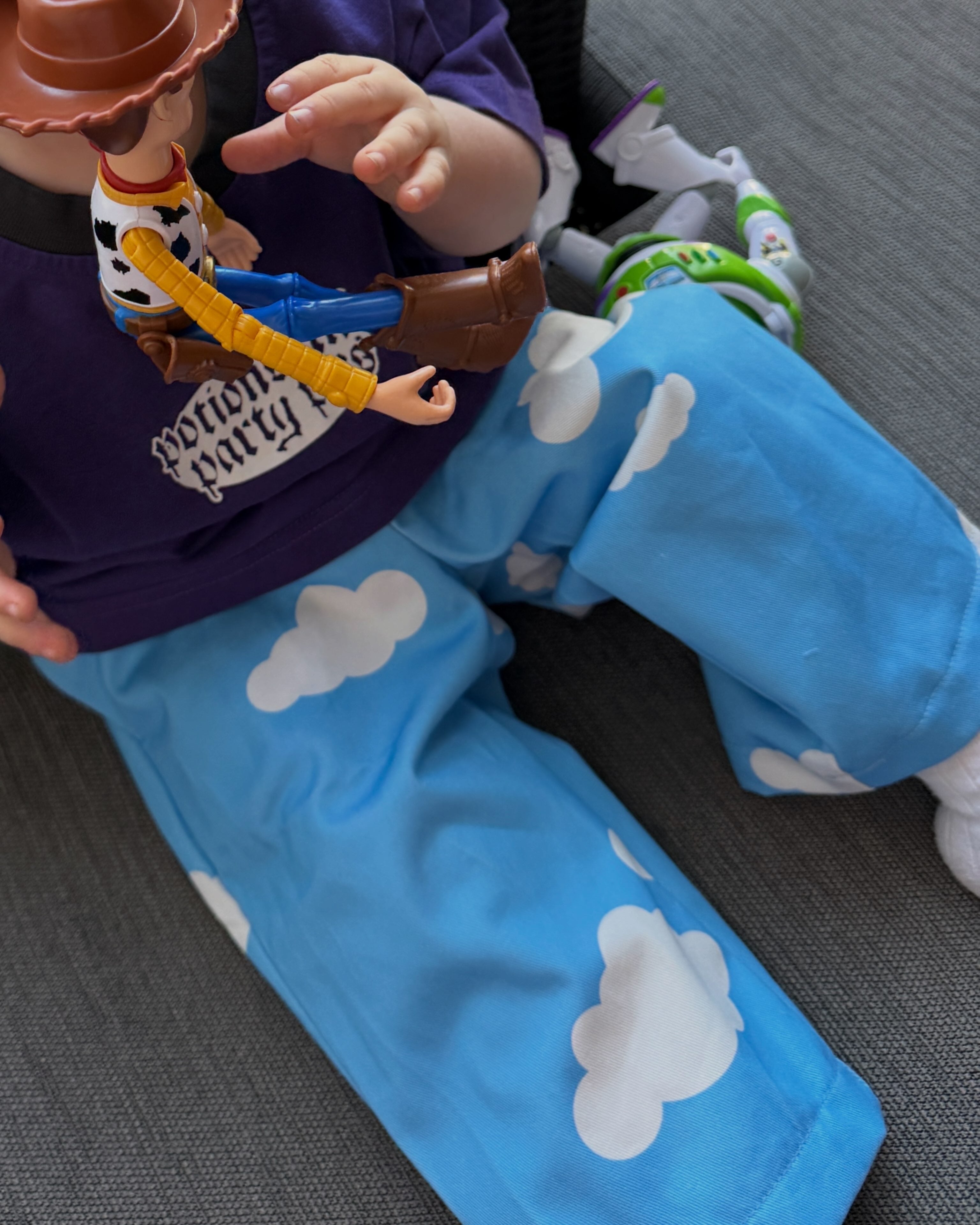 Child wearing blue pants with cloud pattern and a toy figure on a gray surface