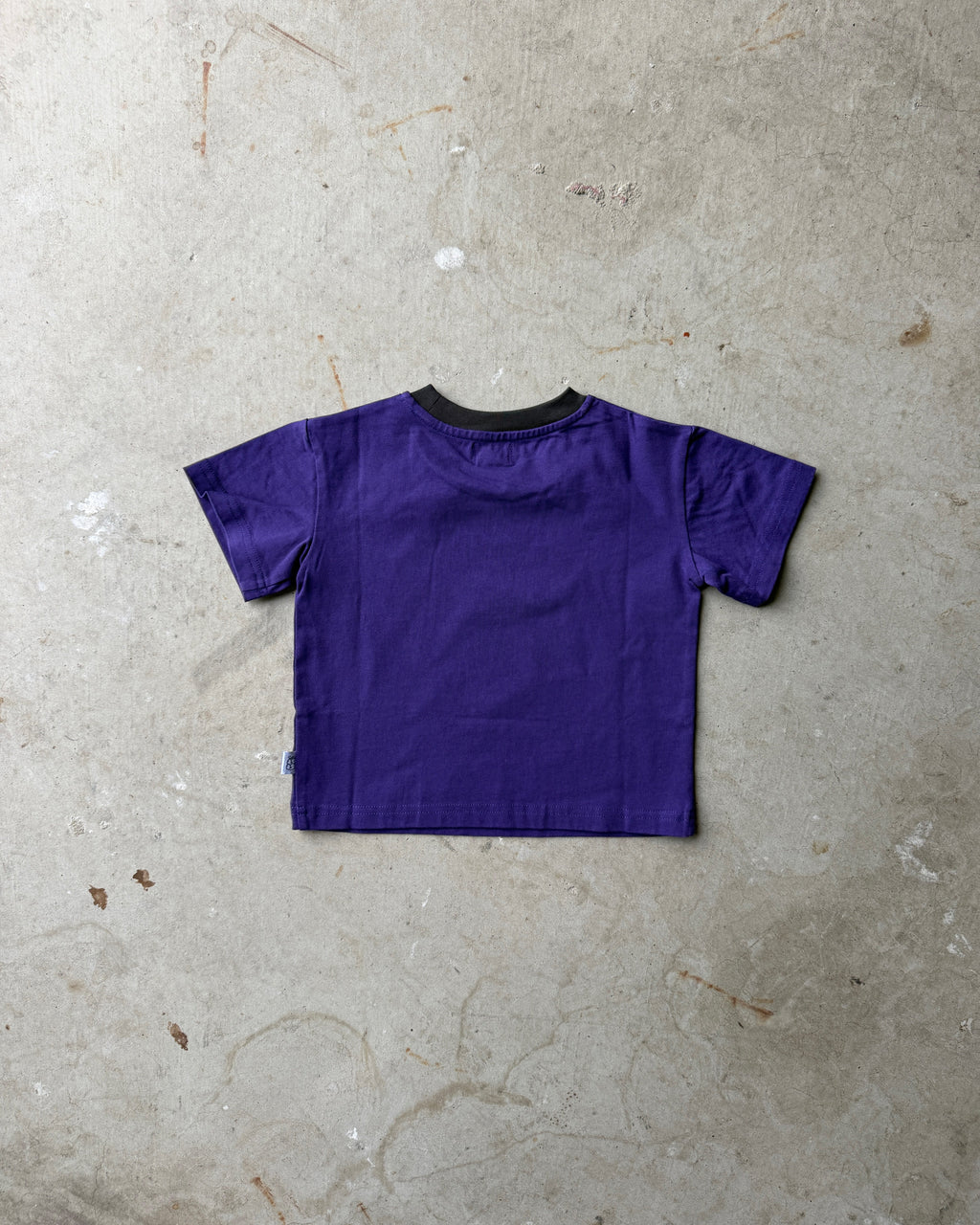 Back of a purple children's t-shirt on a concrete floor