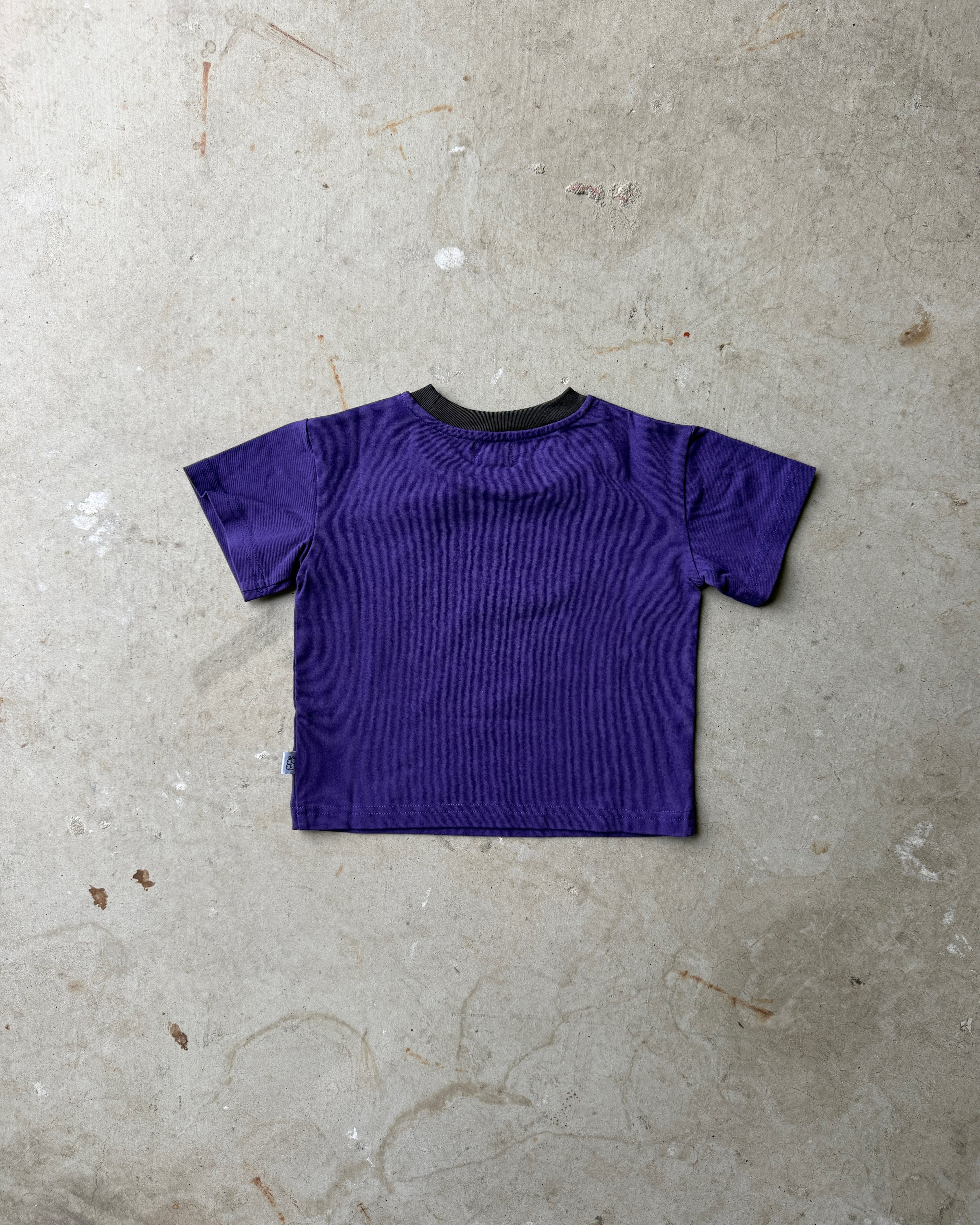 Back of a purple children's t-shirt on a concrete floor