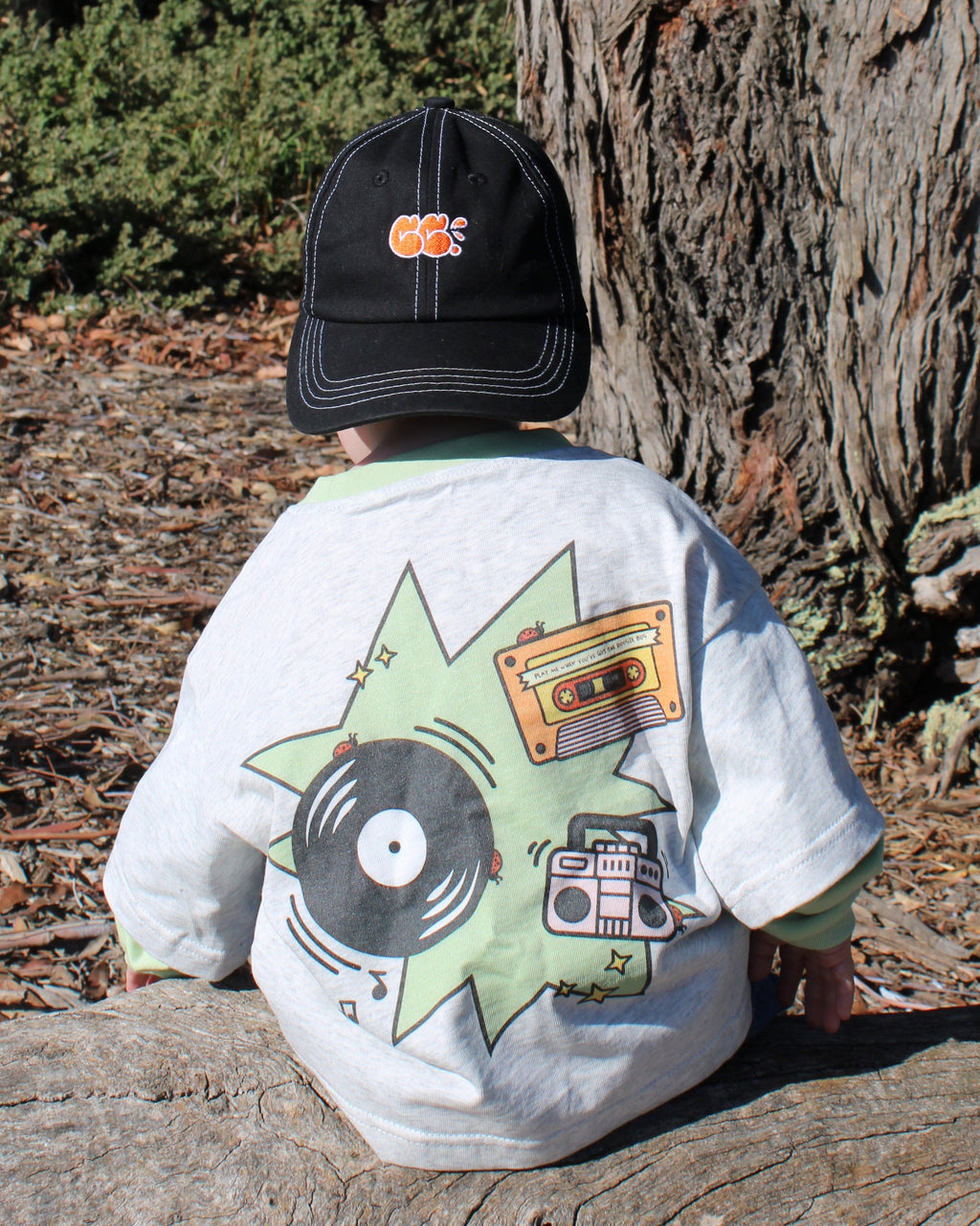 Child wearing a cap and a grey marle shirt with a record player, cassette and boombox design. Long sleeves.