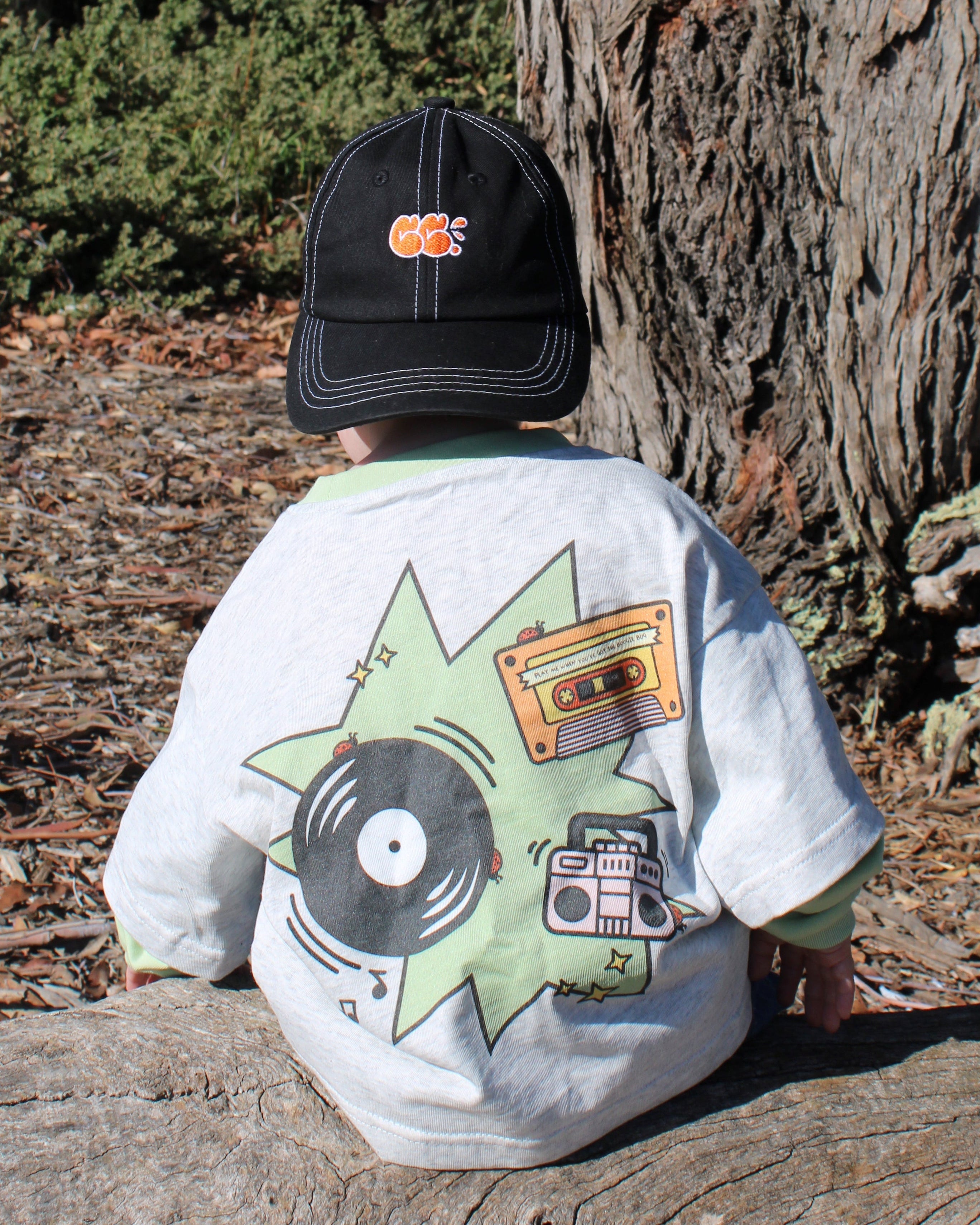 Child wearing a cap and a grey marle shirt with a record player, cassette and boombox design. Long sleeves.