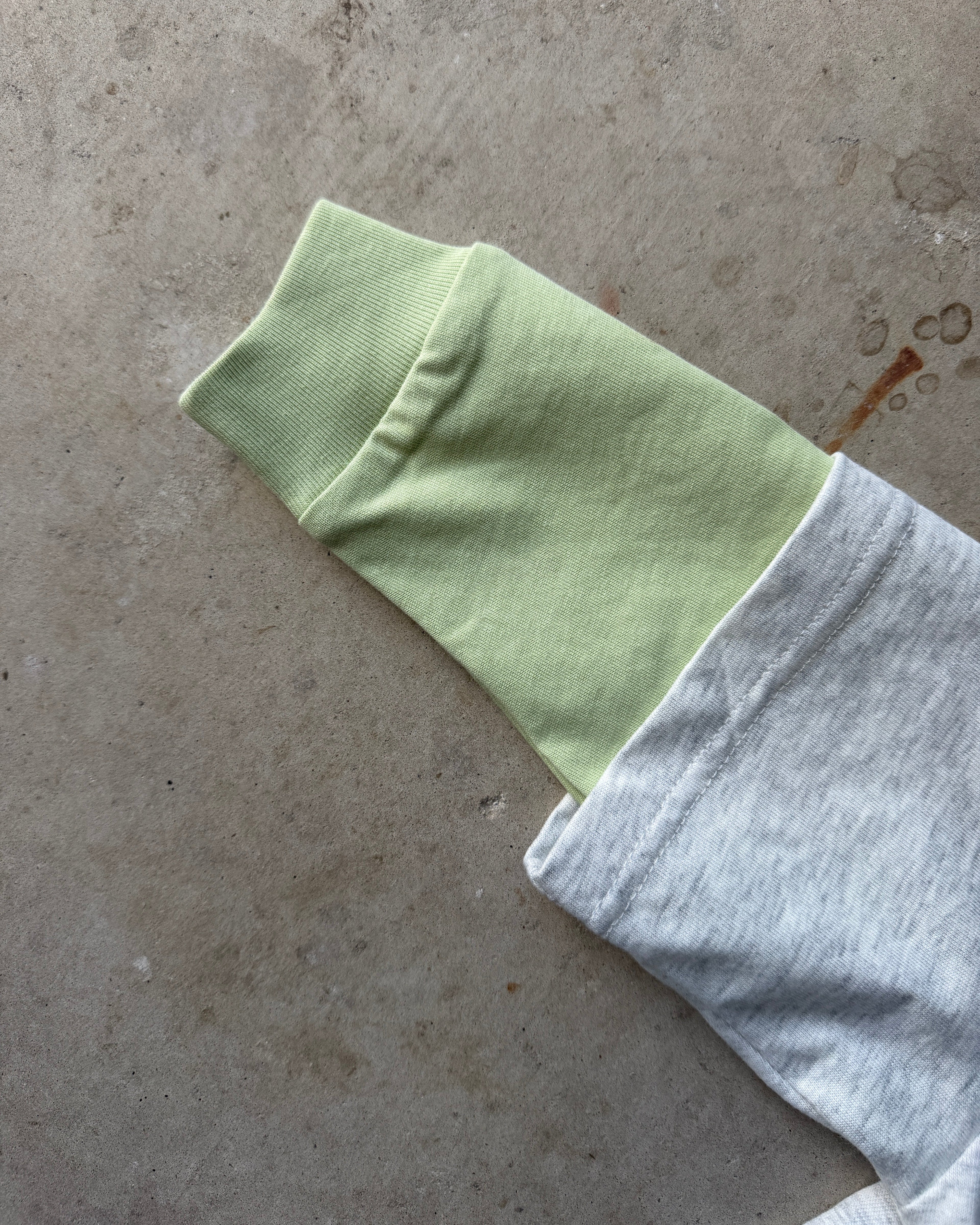 Light green cuff and sleeve with a grey marle tee shirt on a textured concrete surface