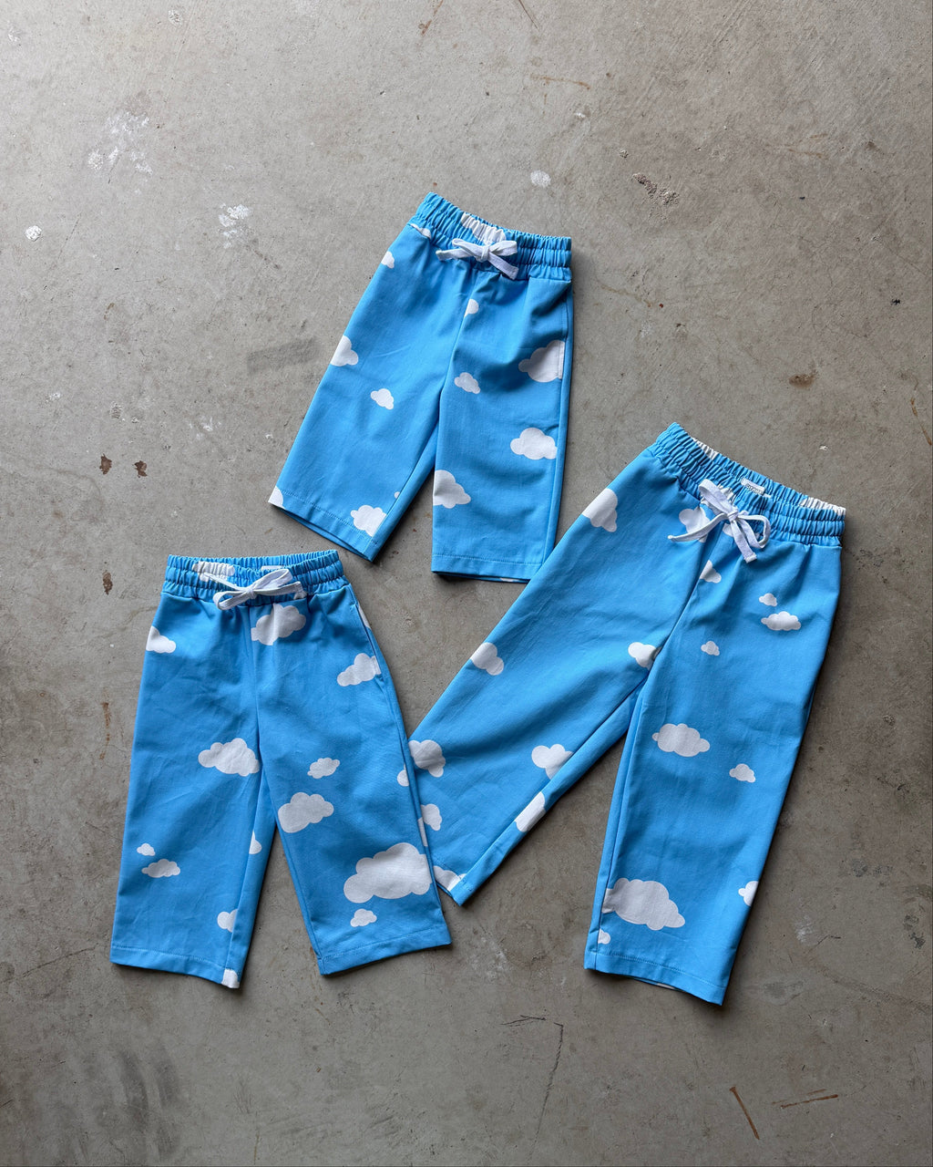 Set of blue children's pants with cloud pattern on a gray concrete floor.