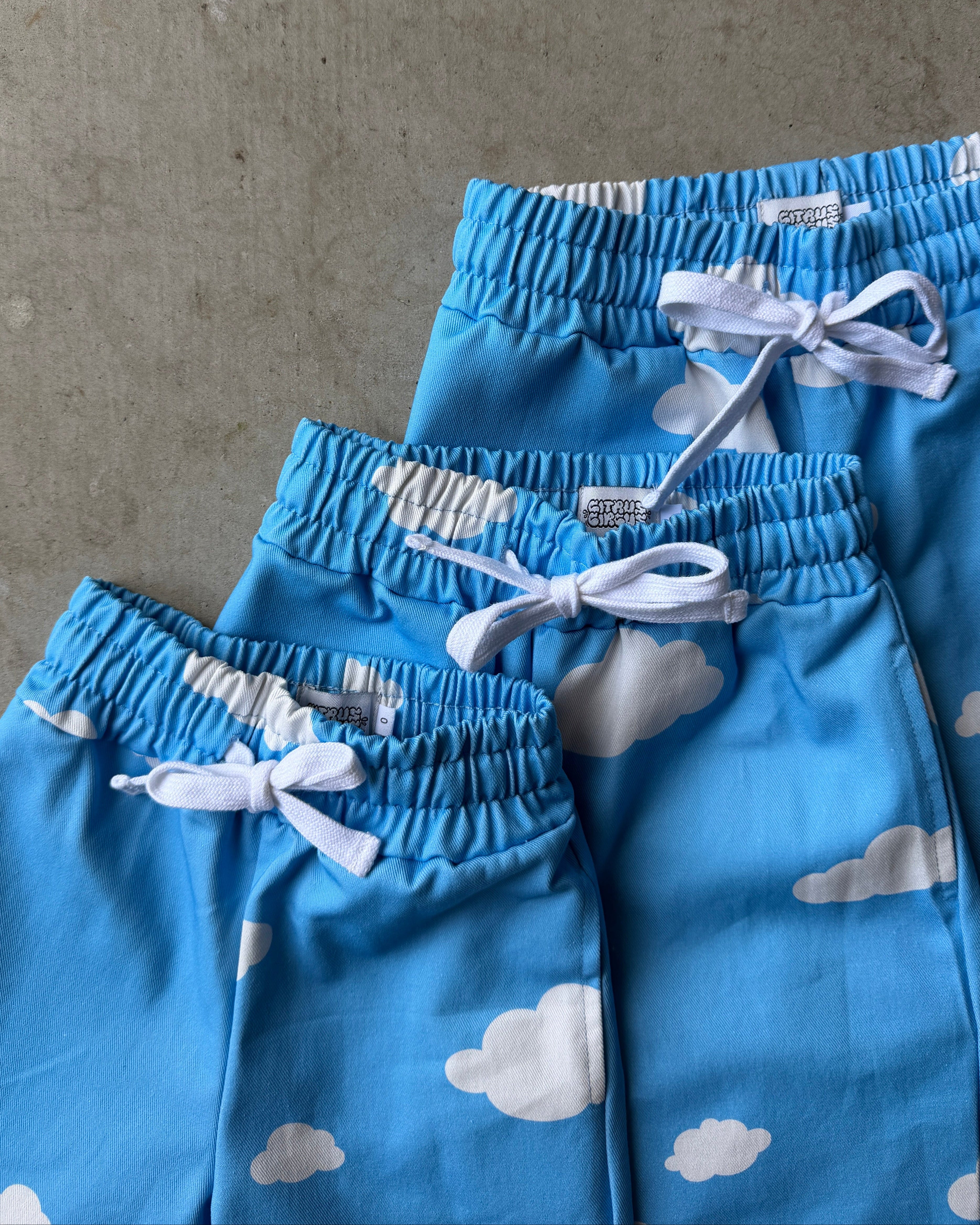 stack of blue children's pants with cloud pattern and white drawstring on a gray concrete surface.