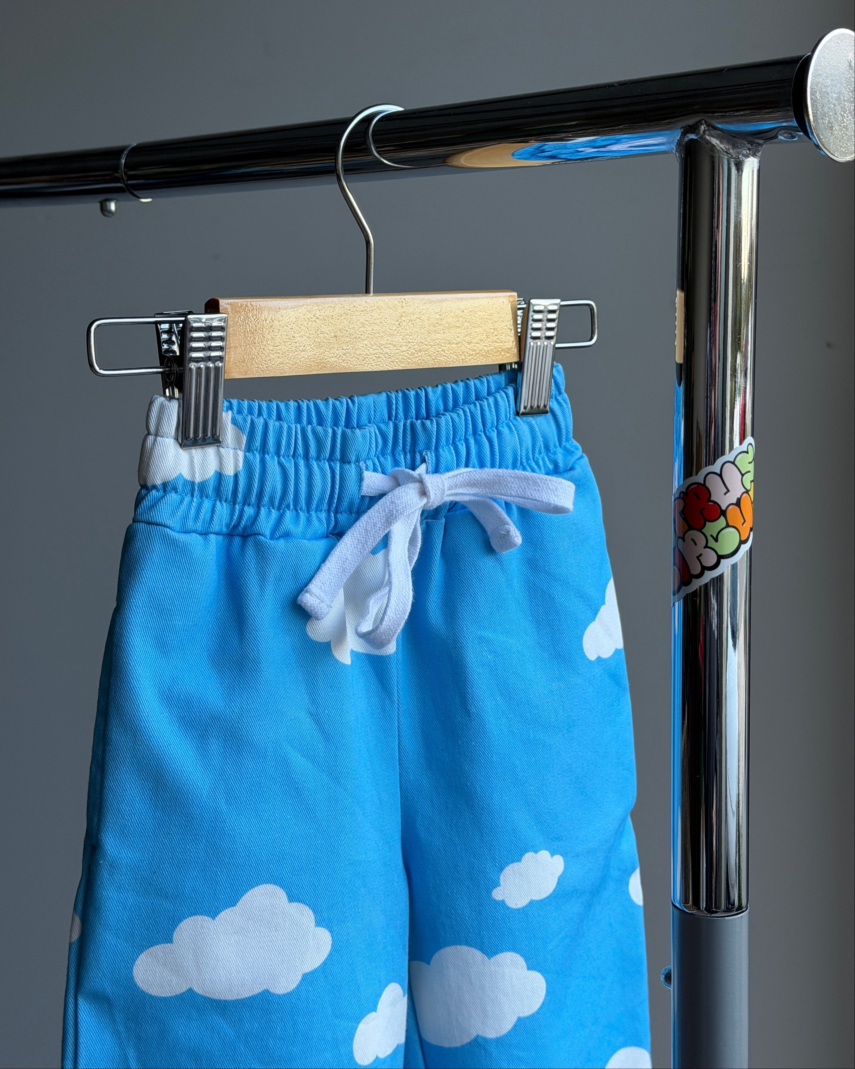 Blue cotton twill pants with cloud pattern hanging on a metal rod against a gray background. Thick, white drawstring.