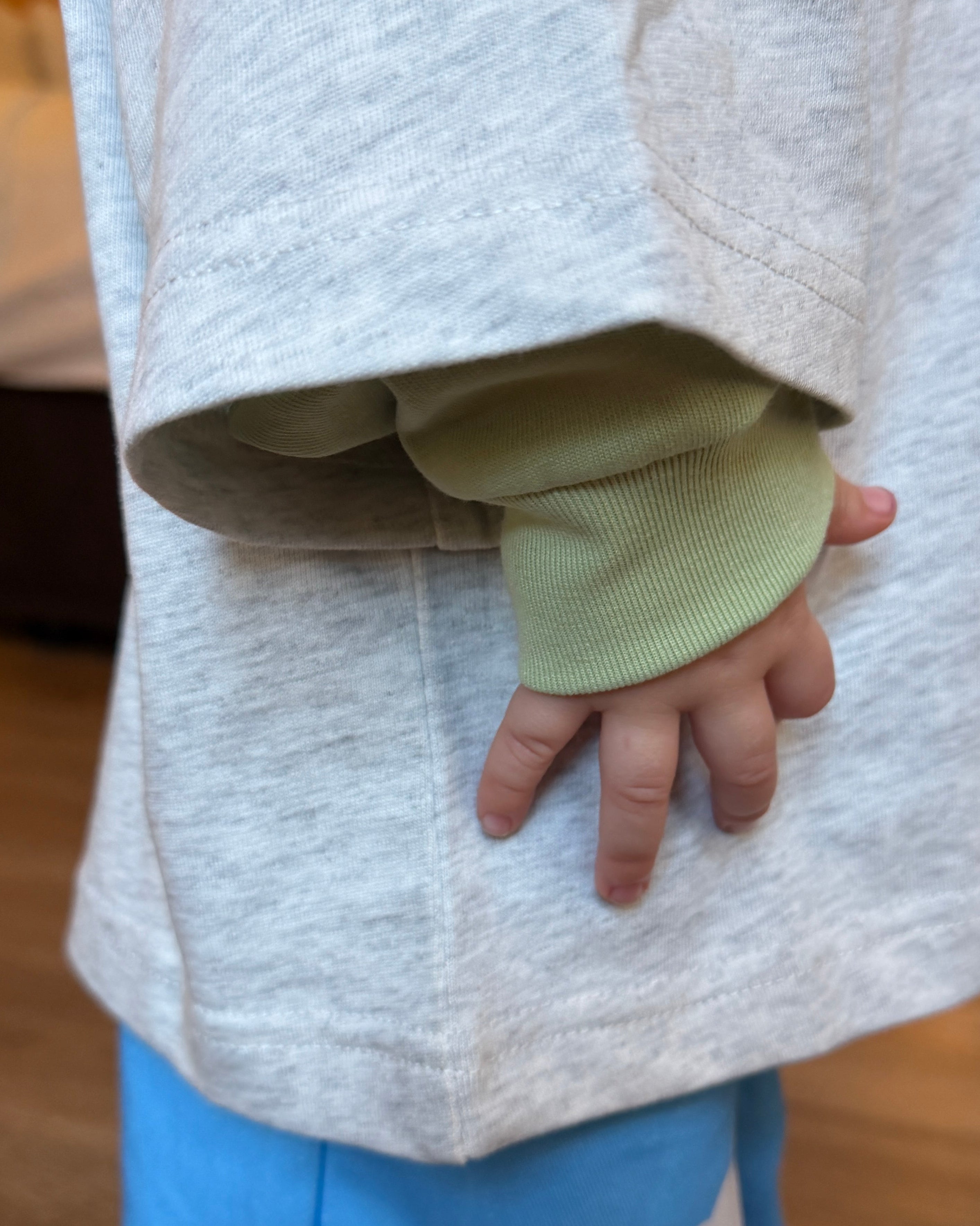 Child's hand in a lime green sleeve with a grey marle t shirt over the top and blue pants.