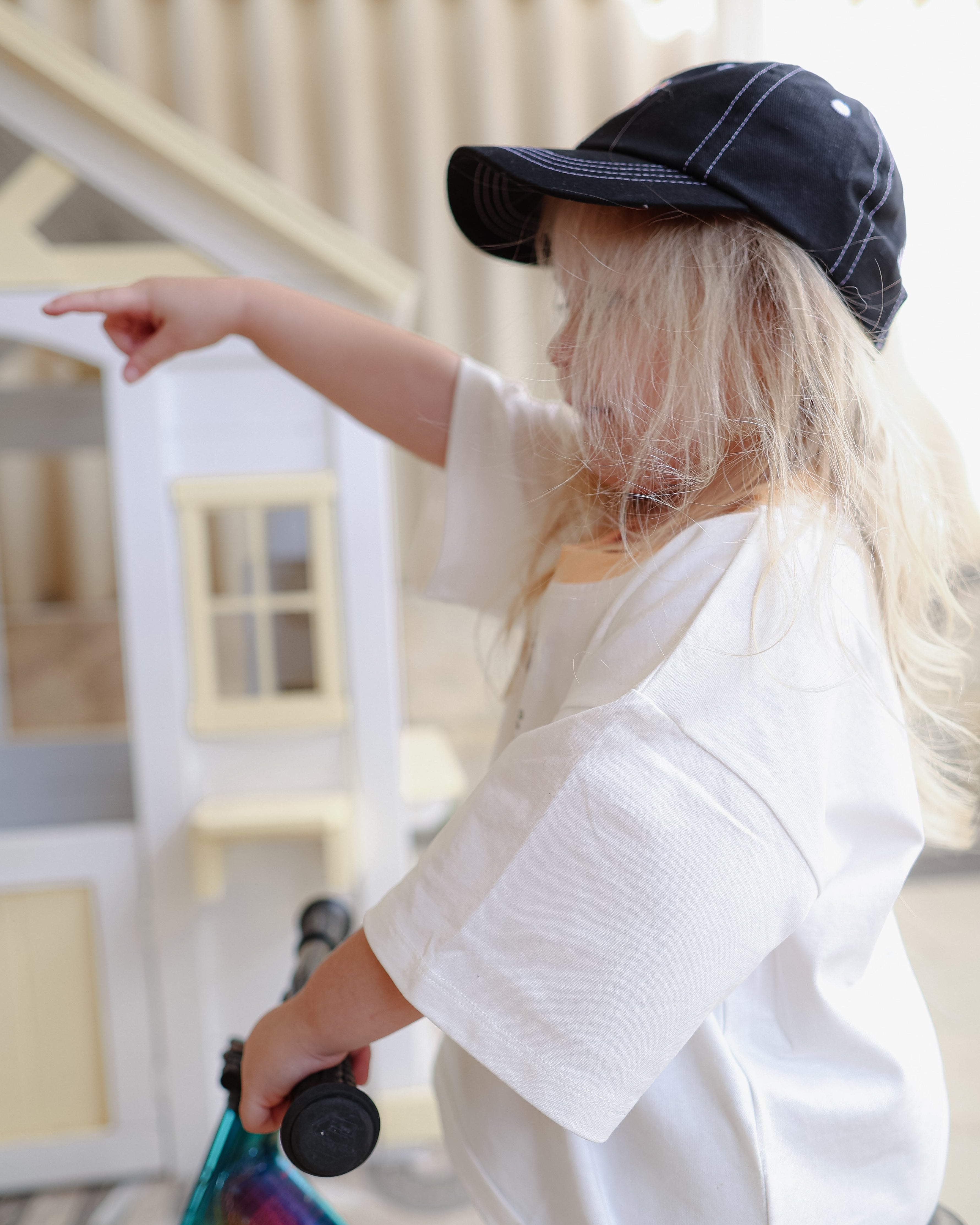 Citrus Circus Starburst OG Tee on child with long hair - oversized kids white tee and black cap white stitching pointing and riding bike
