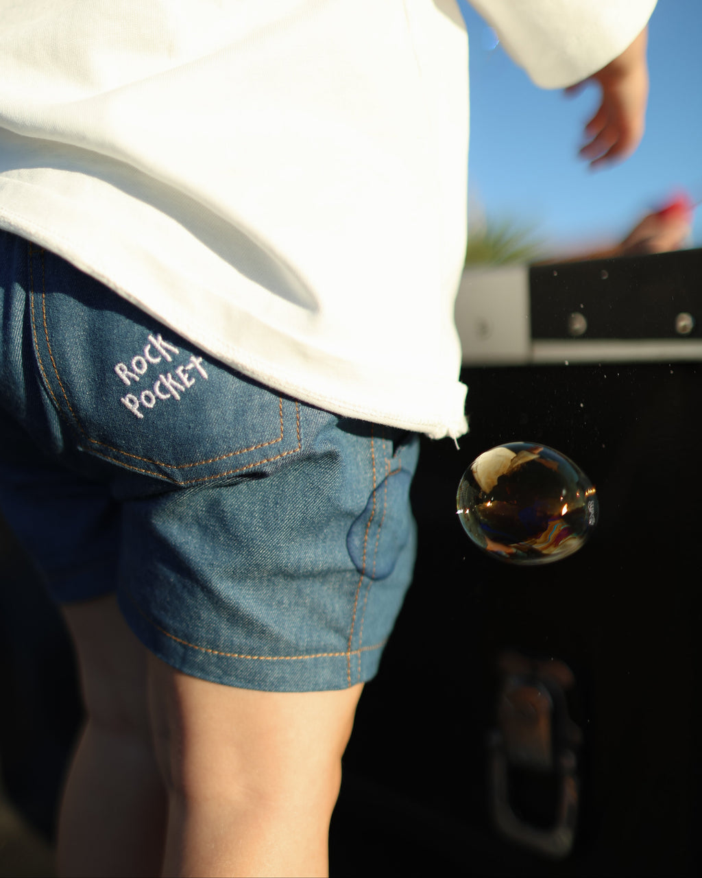 Citrus Circus Rock Pocket Shorts child with bubbles - oversized kids white tee and navy cotton shorts facing backwards