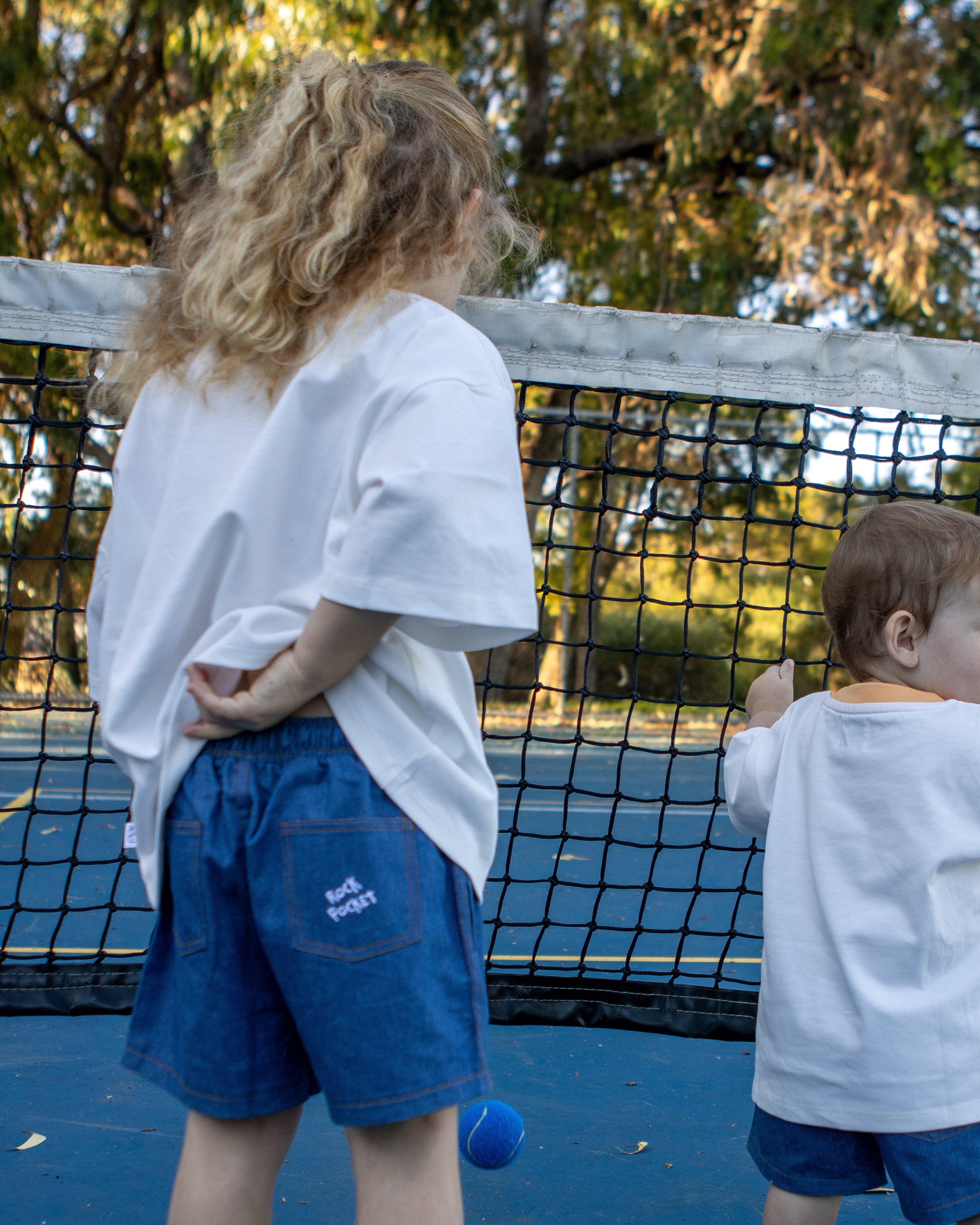 Citrus Circus Starburst OG Tee two children at tennis court - oversized kids white tee and navy cotton shorts