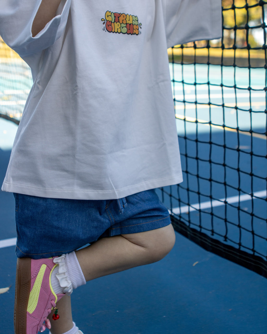 Citrus Circus Starburst OG Tee child at tennis court - oversized kids white tee and navy cotton shorts with pink shoes