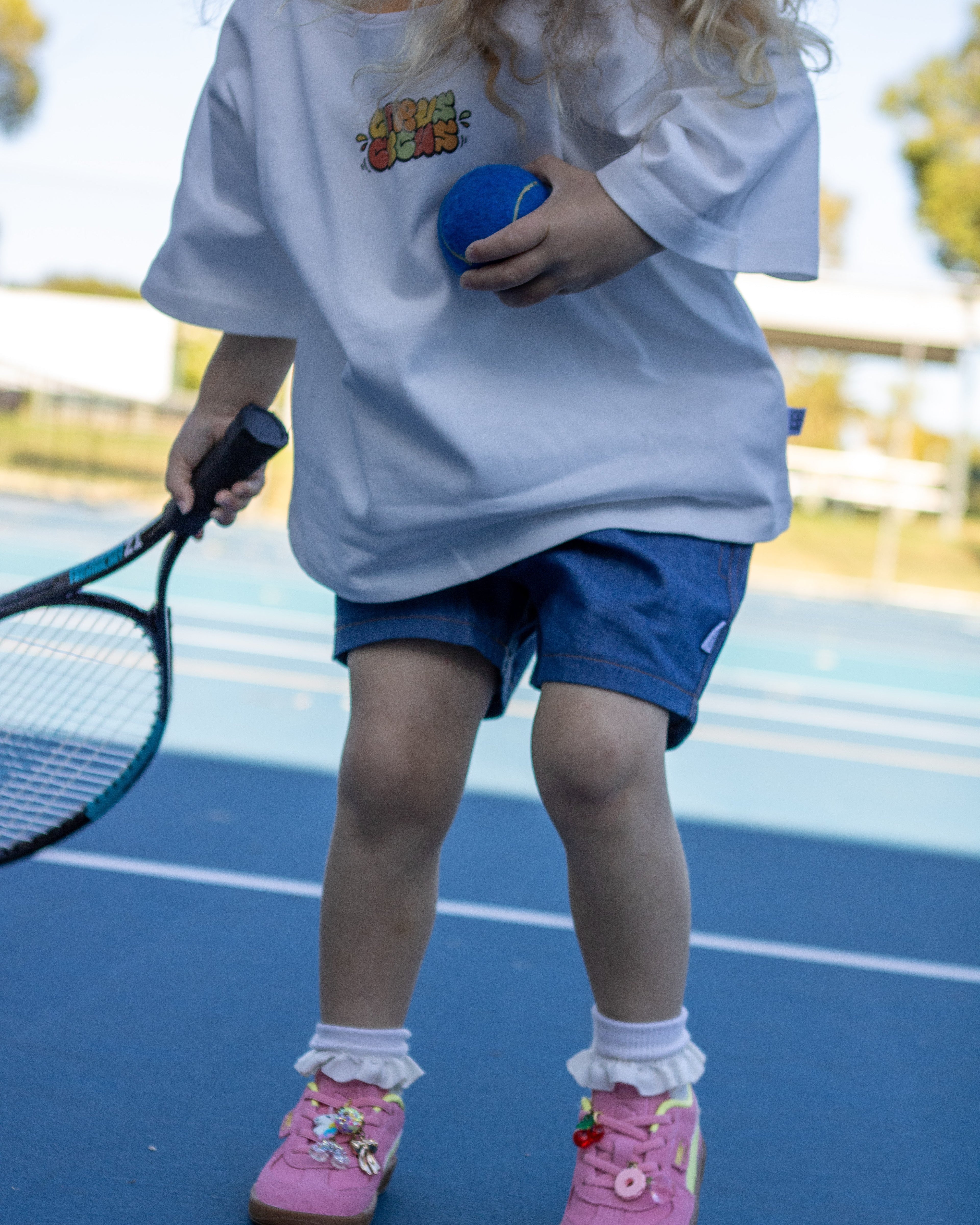 Citrus Circus Starburst OG tee on child at tennis court - oversized kids white tee and navy cotton shorts holding tennis racket and ball