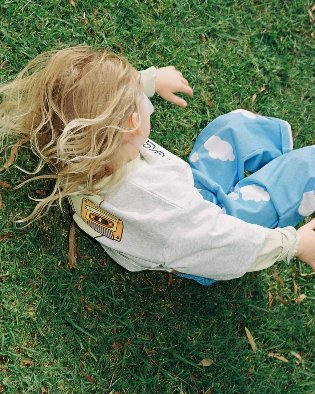 Child lying on grass wearing a grey marle t shirt and blue pants with cloud pattern