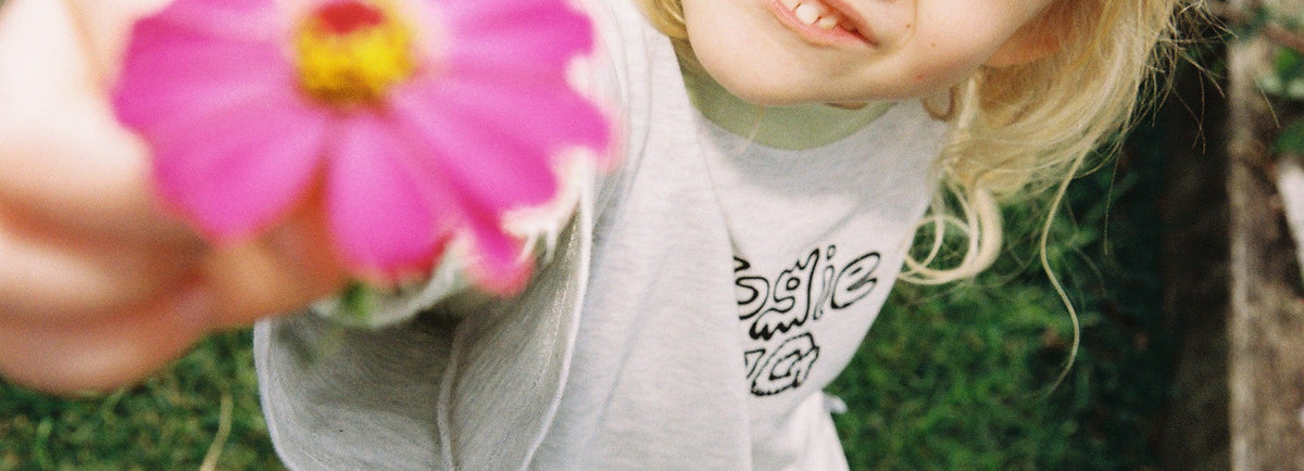 A young child wearing a light gray graphic t-shirt close to the camera, photographed outdoors on a grassy background.