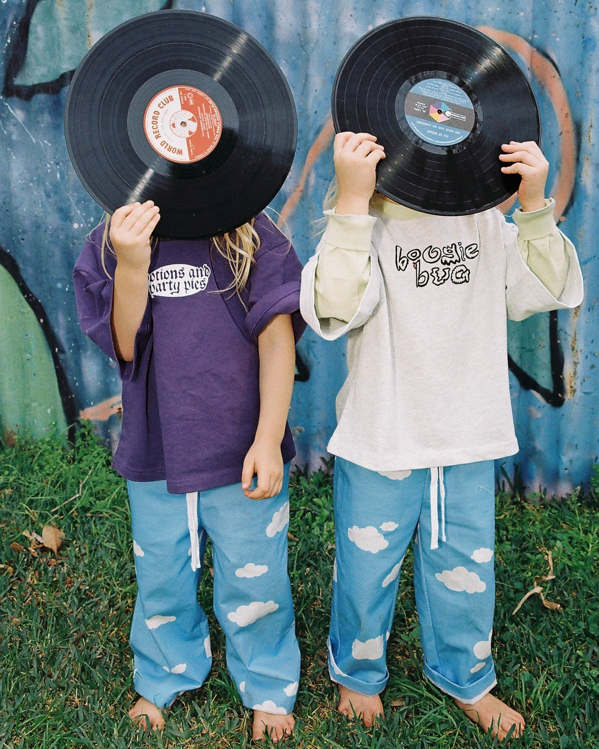 Two children holding vinyl records over their faces against a rustic metal wall.