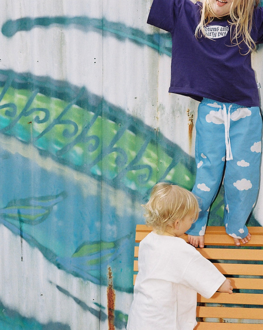 Two children on a wooden bench with a graffiti-covered wall in the background