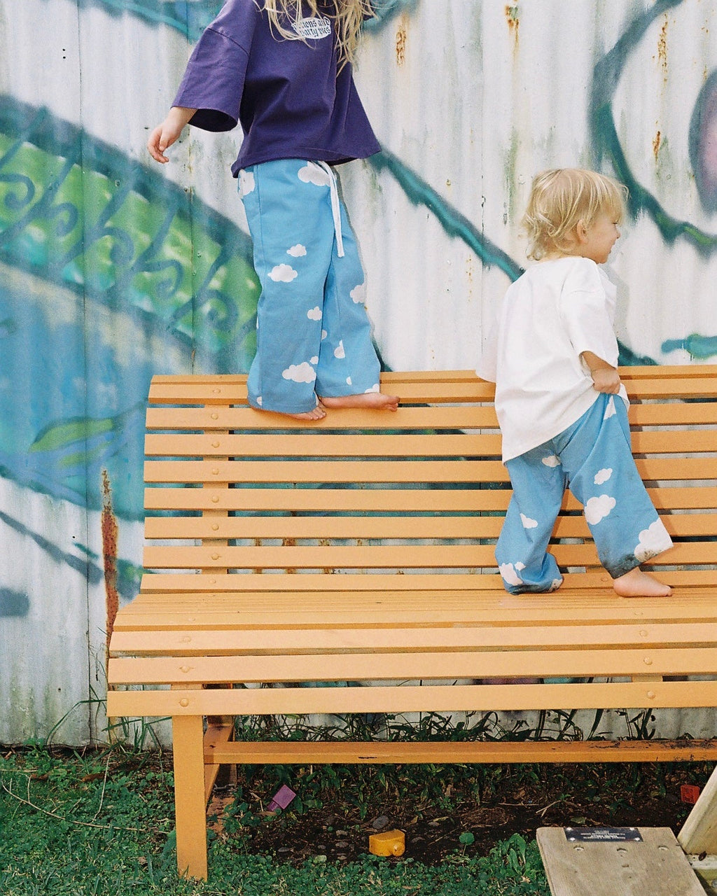Two children standing on a wooden bench with a graffiti-covered wall in the background